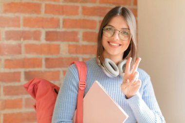 Güzel bir öğrenci gülümsüyor ve arkadaş canlısı görünüyor. İki ya da iki numarayı gösteriyor. Elleri önde, geri sayıyor.