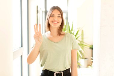 Güzel bir kadın gülümsüyor ve arkadaş canlısı görünüyor. Üç ya da üç numarayı gösteriyor. Elleri önde, geri sayıyor.