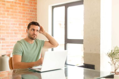 Yakışıklı adam şaşkın ve şaşkın hissediyor, başını kaşıyor ve yana bakıyor.