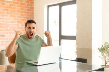 Yakışıklı bir adam sinirli bir ifadeyle ya da yumruklarıyla başarıyı kutlarken agresif bir şekilde bağırıyor.