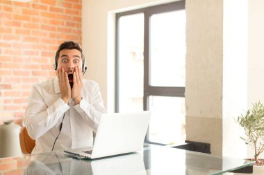 Yakışıklı pazarlamacı şok olmuş ve korkmuş hissediyor, ağzı açık ve elleri yanaklarında korkmuş görünüyor.