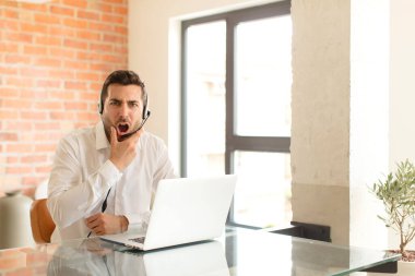 Ağzı ve gözleri açık, eli çenesinde olan yakışıklı bir pazarlamacı. Kötü bir şok geçiriyor.