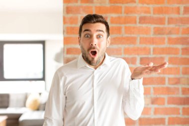Yakışıklı işadamı şaşırmış ve şok olmuş görünüyor, çenesi düşmüş ve eli açık bir nesneyi tutuyor.