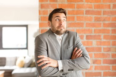 Yakışıklı iş adamı omuz silkiyor, şaşkın ve kararsız hissediyor, kolları bağlı ve şaşkın bir şekilde şüpheye düşüyor.