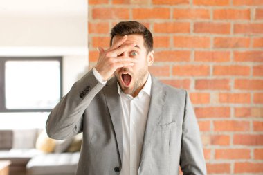 Yakışıklı iş adamı, şok olmuş, korkmuş ya da korkmuş görünüyor. Yüzü elle kaplanmış ve parmaklarının arasından gizlice bakıyor.