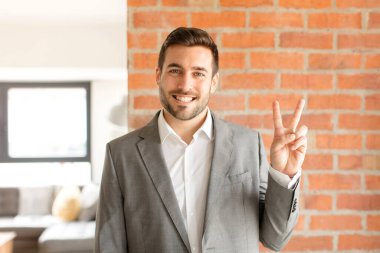 Yakışıklı iş adamı gülümsüyor ve arkadaş canlısı görünüyor. İki ya da iki numarayı gösteriyor. Elleri önde, geri sayıyor.