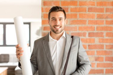 Yakışıklı mimar mutlu bir şekilde gülümsüyor, eli kalçasında ve kendinden emin, olumlu, gururlu ve arkadaş canlısı.