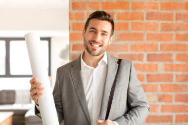 Yakışıklı mimar kameraya bakıyor, kendinden emin, arkadaş canlısı bir gülümsemeyle, seni seçiyor.