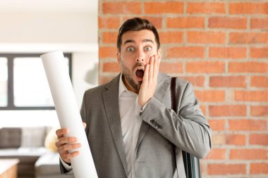 Yakışıklı mimar şok olmuş ve korkmuş hissediyor, ağzı açık ve elleri yanaklarında korkmuş görünüyor.