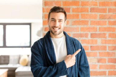 Yakışıklı adam neşeyle gülümsüyor, mutlu hissediyor ve yan ve yukarı doğru işaret ediyor, fotokopi uzayındaki nesneleri gösteriyor.