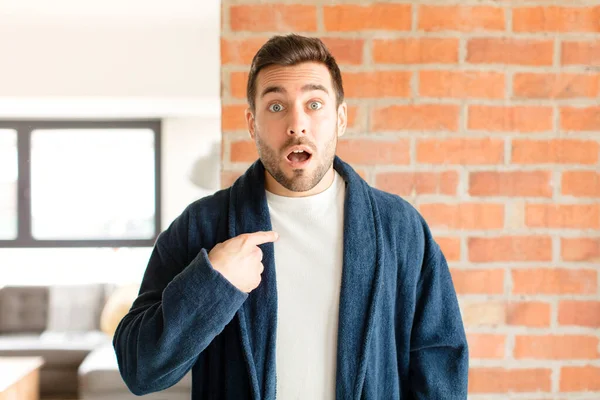 Yakışıklı adam şaşkın ve şaşkın görünüyor, ağzı açık, kendini işaret ediyor.