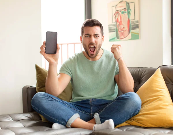 Yakışıklı bir adam sinirli bir ifadeyle ya da yumruklarıyla başarıyı kutlarken agresif bir şekilde bağırıyor.