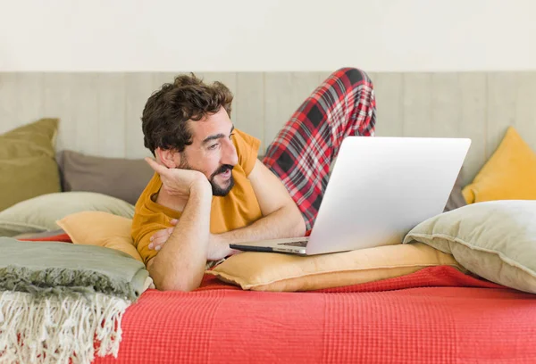 young bearded man on a bed with a laptop