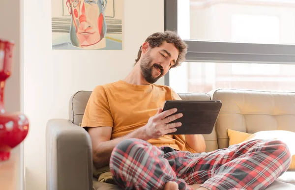 Kanepedeki sakallı genç adam Dokunmatik ekranlı tabletle