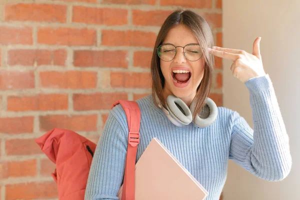 pretty student looking unhappy and stressed, suicide gesture making gun sign with hand, pointing to head