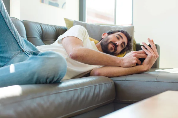 Genç Sakallı Adam Akıllı Telefonuyla Kanepede Dinleniyor — Stok fotoğraf