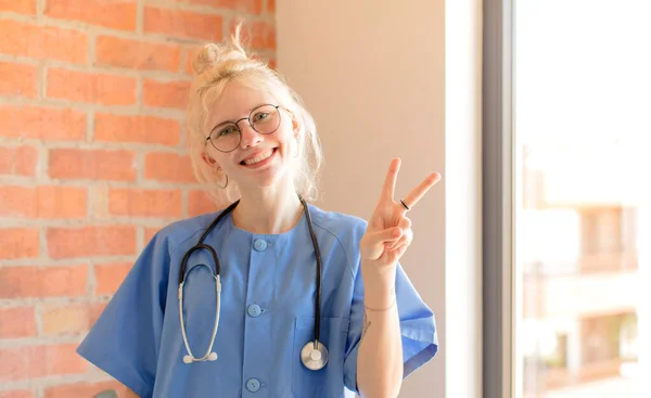 Ładna Pielęgniarka Uśmiecha Się Wygląda Przyjaźnie Pokazuje Numer Dwa Lub — Zdjęcie stockowe