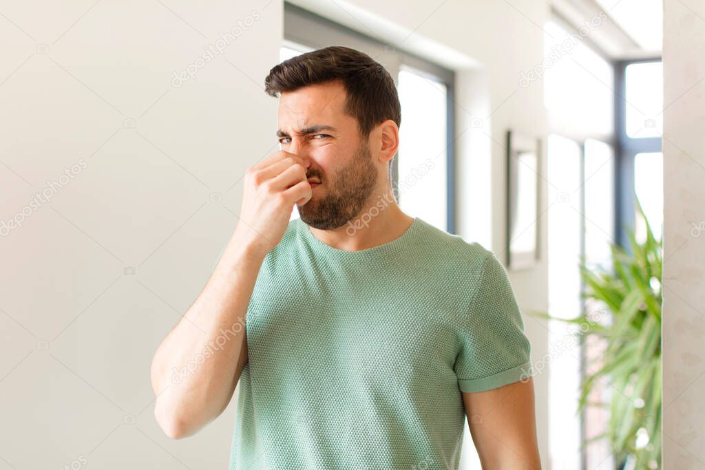 handsome man feeling disgusted, holding nose to avoid smelling a foul and unpleasant stench