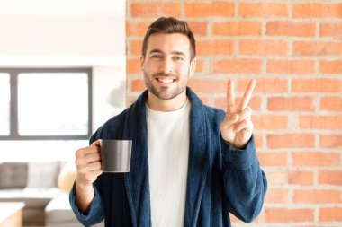 Yakışıklı adam gülümsüyor ve arkadaş canlısı görünüyor. İki ya da iki numarayı gösteriyor. Elleri önde, geriye doğru sayıyor.