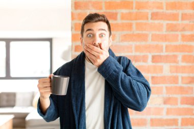 Yakışıklı bir adam elleri ile ağzını kapatıyor, şok olmuş, şaşırmış bir ifadeyle, sır saklıyor ya da 