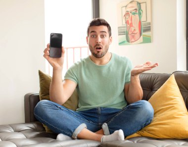 Yakışıklı adam şaşırmış ve şoka uğramış görünüyor, çenesi düşmüş, bir objeyi elinde açık bir elle tutuyor.