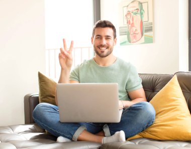 Yakışıklı adam gülümsüyor ve mutlu görünüyor, kaygısız ve pozitif, işaret eden zafer ya da barış tek elle