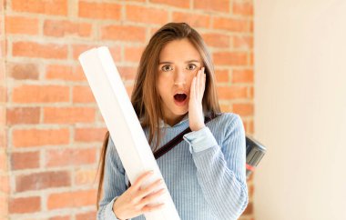 Güzel mimar şok olmuş ve korkmuş hissediyor, ağzı açık ve elleri yanaklarında korkmuş görünüyor.