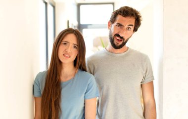 young couple feeling puzzled and confused, with a dumb, stunned expression looking at something unexpected