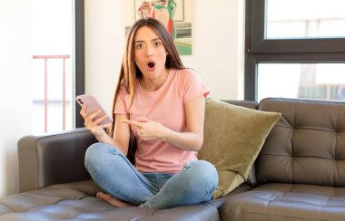 Güzel bir kadın inançsızlıktan şaşkın şaşkın bakıyor, yan taraftaki objeyi işaret ediyor ve diyor ki: