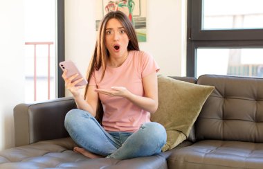 Güzel bir kadın şaşırmış ve şoka uğramış görünüyor, çenesi düşmüş, elinde açık bir elle bir nesne tutuyor.