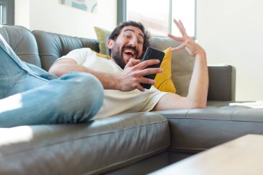 Genç sakallı adam akıllı telefonuyla kanepede dinleniyor.