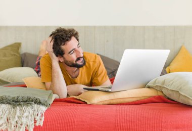 Yatakta dizüstü bilgisayarlı genç sakallı bir adam.