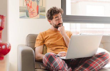 Kanepede dizüstü bilgisayarlı genç sakallı bir adam.