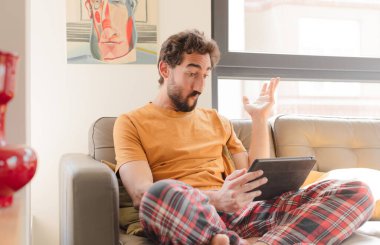 Kanepedeki sakallı genç adam Dokunmatik ekranlı tabletle