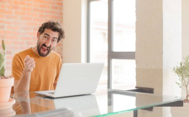 Evde dizüstü bilgisayarla çalışan sakallı genç bir adam.