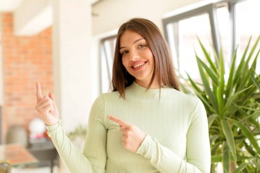 Güzel bir kadın mutlu bir şekilde gülümsüyor ve her iki elini de fotokopi uzayında nesne göstererek yukarı ve yana doğru işaret ediyor.