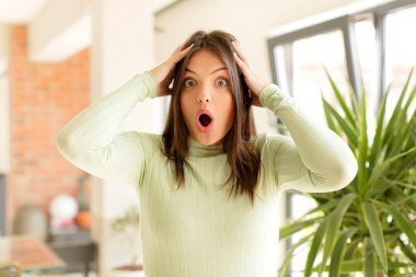 Güzel bir kadın heyecanlı ve şaşırmış görünüyor, ağzı açık, elleri başının üstünde, şanslı bir kazanan gibi hissediyor.