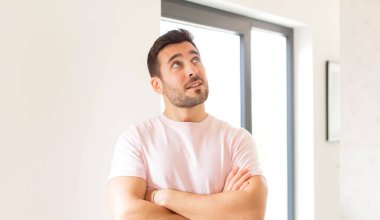 Yakışıklı adam kendini mutlu, gururlu ve umutlu hissediyor, merak ediyor ya da düşünüyor, çapraz kollarla uzayı taklit ediyor.