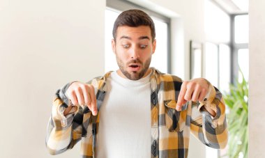 Yakışıklı ve ağzı açık bir adam iki eliyle aşağıya bakıyor. Şok olmuş, şaşırmış ve şaşırmış görünüyor.