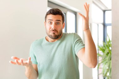 handsome man shrugging with a dumb, crazy, confused, puzzled expression, feeling annoyed and clueless