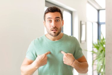 Yakışıklı bir adam, kafası karışmış ve tuhaf bakışlarıyla kendini işaret ediyor. Seçildiğine şaşırmış ve şaşırmış.