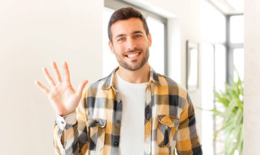 Yakışıklı adam gülümsüyor ve arkadaş canlısı görünüyor, 5 ya da 5 numarayı gösteriyor, eli önde, geri sayıyor.