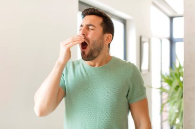 Yakışıklı adam sabahın köründe uykulu, yorgun ve sıkkın bir şekilde esniyor.