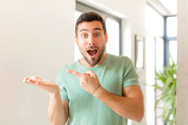 Yakışıklı adam neşeyle gülümsüyor ve yan taraftaki fotokopi alanını gösteriyor, bir nesneyi gösteriyor ya da reklamını yapıyor.