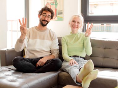 Genç çift gülümsüyor ve arkadaş canlısı görünüyor. Elleri önde ve geriye doğru sayıyor.
