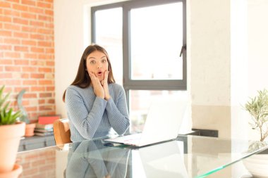 Güzel kadın şok olmuş ve korkmuş hissediyor, ağzı açık ve elleri yanaklarında korkmuş görünüyor.