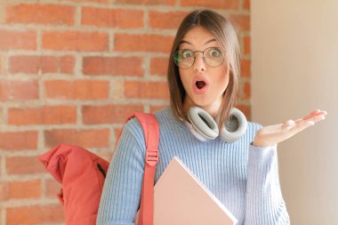 Güzel bir öğrenci şaşırmış ve şok olmuş görünüyor, çenesi düşmüş, bir objeyi elinde açık bir elle tutuyor.