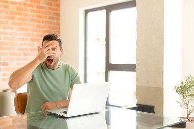 Yakışıklı adam şok olmuş, korkmuş ya da korkmuş görünüyor. Yüzü elle kaplanmış ve parmaklarının arasından gizlice bakıyor.