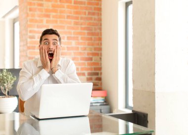 Yakışıklı iş adamı şok olmuş ve korkmuş hissediyor, ağzı açık ve elleri yanaklarında korkmuş görünüyor.