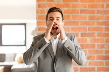 Yakışıklı iş adamı mutlu, heyecanlı ve pozitif hissediyor. Elleri ağızda, bağırarak bağırıyor.